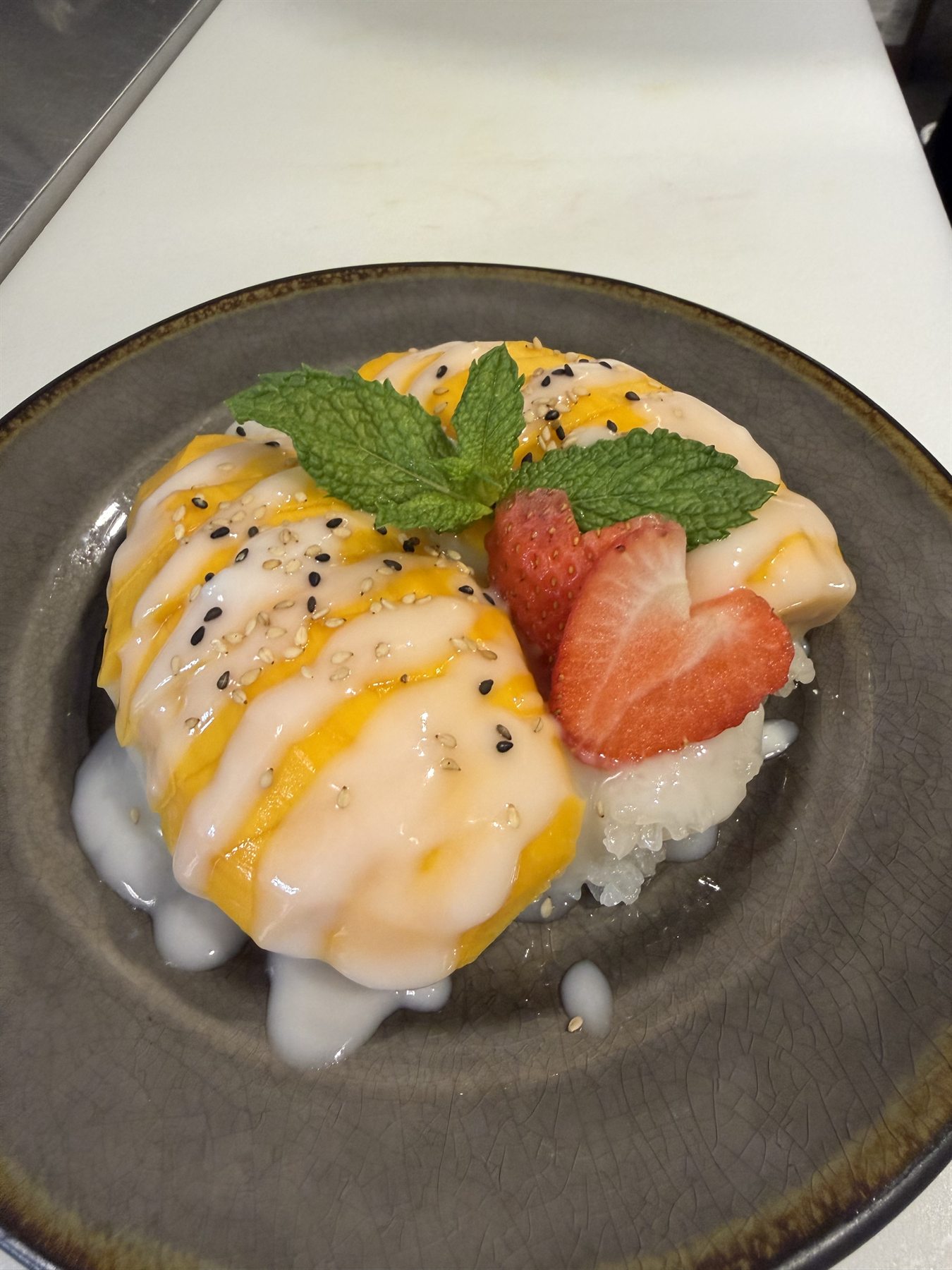 Mango sticky rice with coconut cream, garnished with strawberry and mint