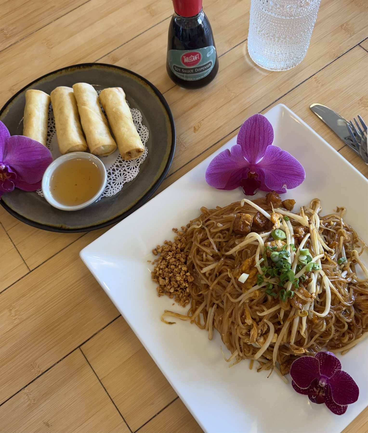 Pad Thai noodles topped with bean sprouts and crushed peanuts, plated with crispy spring rolls