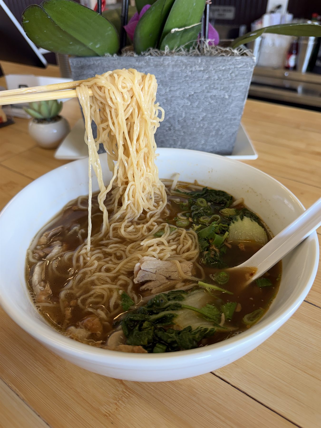 Bowl of beef pho noodle soup with fresh herbs and chopsticks lifting the noodles